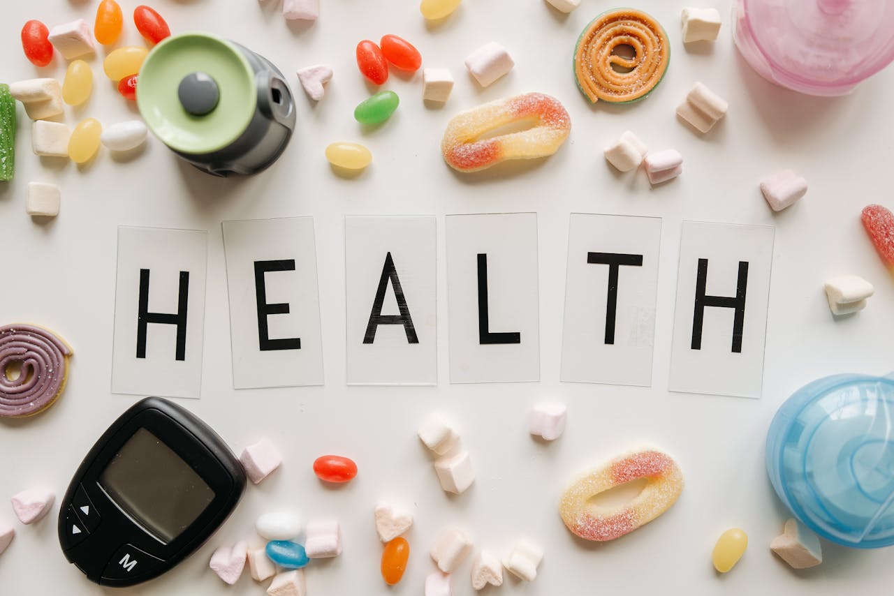Creative flat lay with sweets around a 'HEALTH' text and monitoring device, symbolizing diabetes awareness.